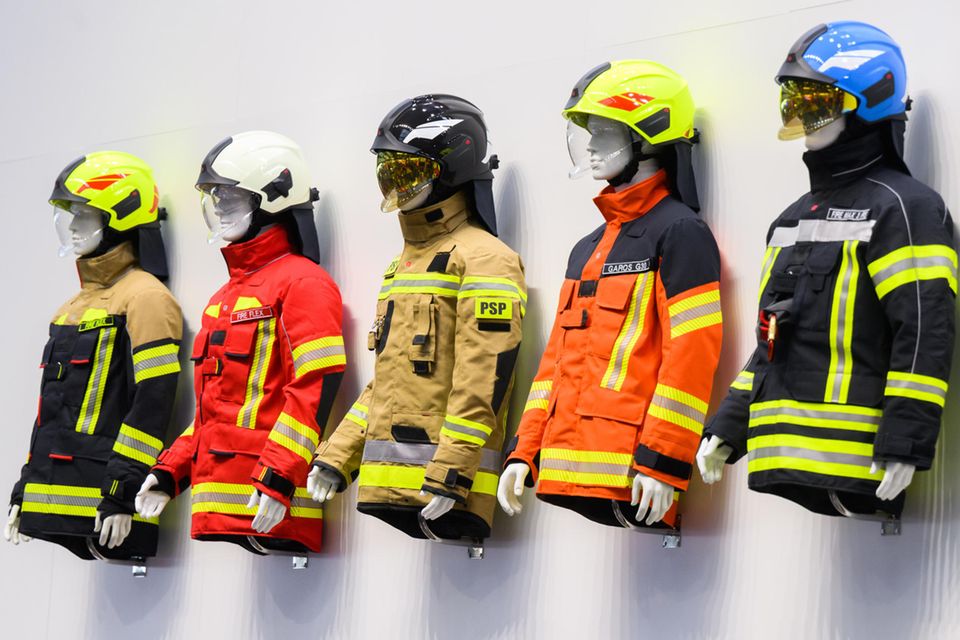 Puppen mit Helmen und Schutzjacken hängen bei der Interschutz am Messestand von Rosenbauer