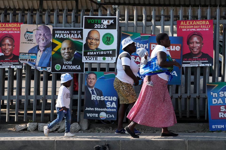 Menschen gehen an einer Wand mit Wahlplakaten vorbei