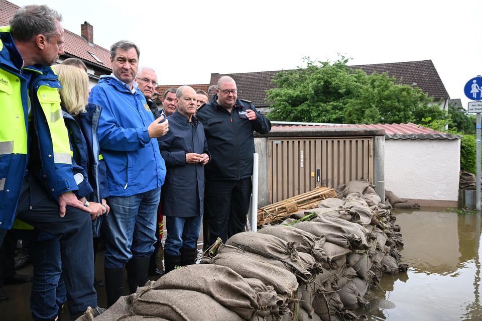 Markus Söder und Olaf Scholz stehen in Gummistiefeln hinter Sandsäcken vor den Starkregen-Fluten.