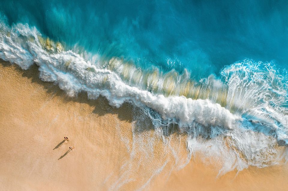 Ein Pärchen läuft am Strand in Bali hohe wellen spülen durch den Sand