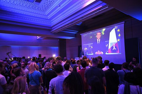 Präsident Macron ist auf einer Leinwand bei einer Ansprache zu sehen