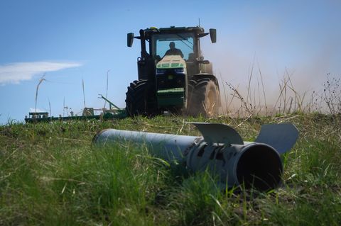 Ein Bruchstück einer russischen Rakete ist im Vordergrund zu sehen, während ein Bauer auf seinem Feld in Izium arbeitet