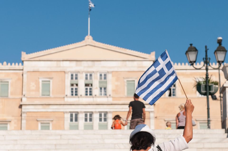 Eine steht mit einer griechischen Flagge in der Hand vor dem Parlament in Athen