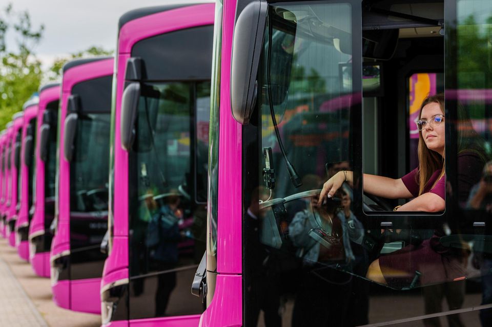 Eine Busfahrerin sitzt am Steuer ihres Busses und schaut aus dem geöffneten Fenster