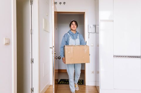 Junge Frau trägt einen Umzugskarton in eine Wohnung