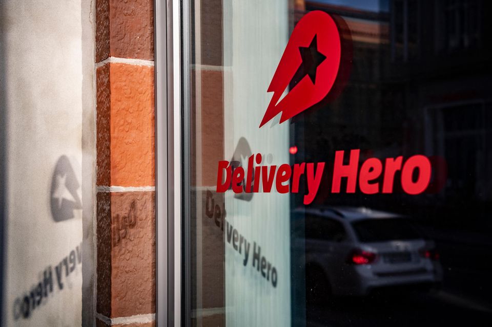 Logo und der Schriftzug des Essenslieferdienstes Delivery Hero spiegelt sich in einer Fensterscheibe am Firmensitz