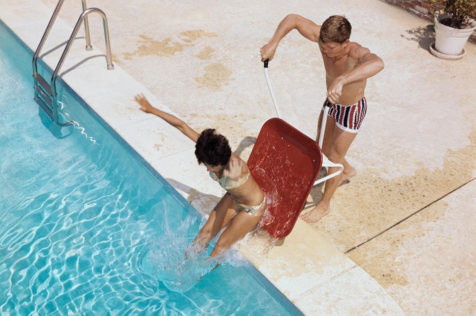 Ein Junge schubst ein Mädchen mit einer Schubkarre in einen Swimmingpool