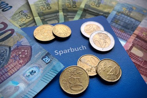 Ein Sparbuch mit Geldscheinen und Münzen obendrauf