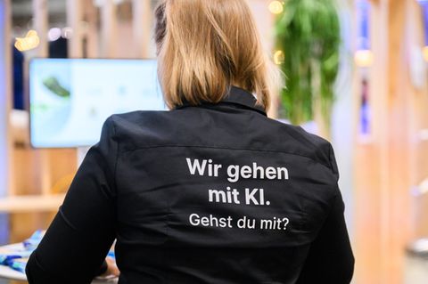 Eine Frau steht mit einem Shirt mit Aufschrift „Wir gehen mit KI. Gehst du mit?“ am Messestand von Google