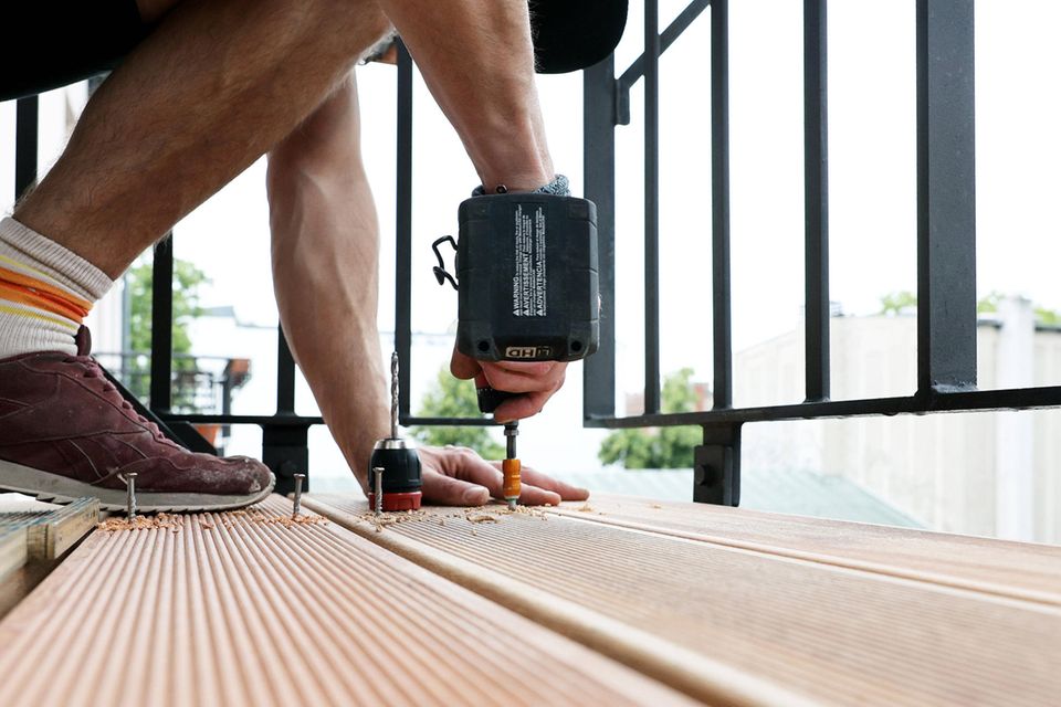 Ein Balkon wird mit Holzbohlen bestückt, sie werden mit Schrauben fixiert
