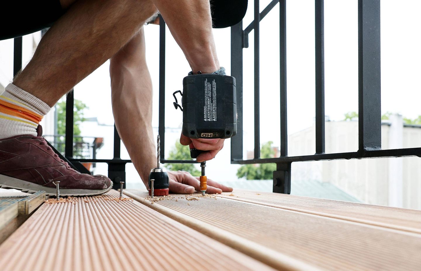Ein Balkon wird mit Holzbohlen bestückt, sie werden mit Schrauben fixiert