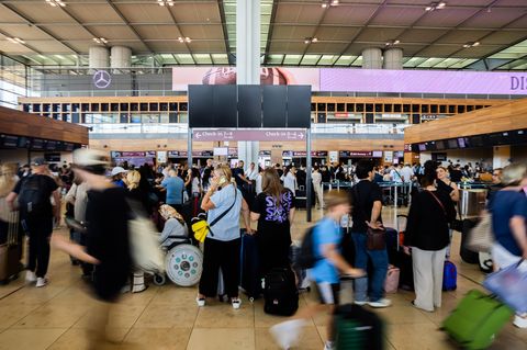 Zahlreiche Fluggäste warten am Hauptstadtflughafen BER vor einer schwarzen Anzeigetafel