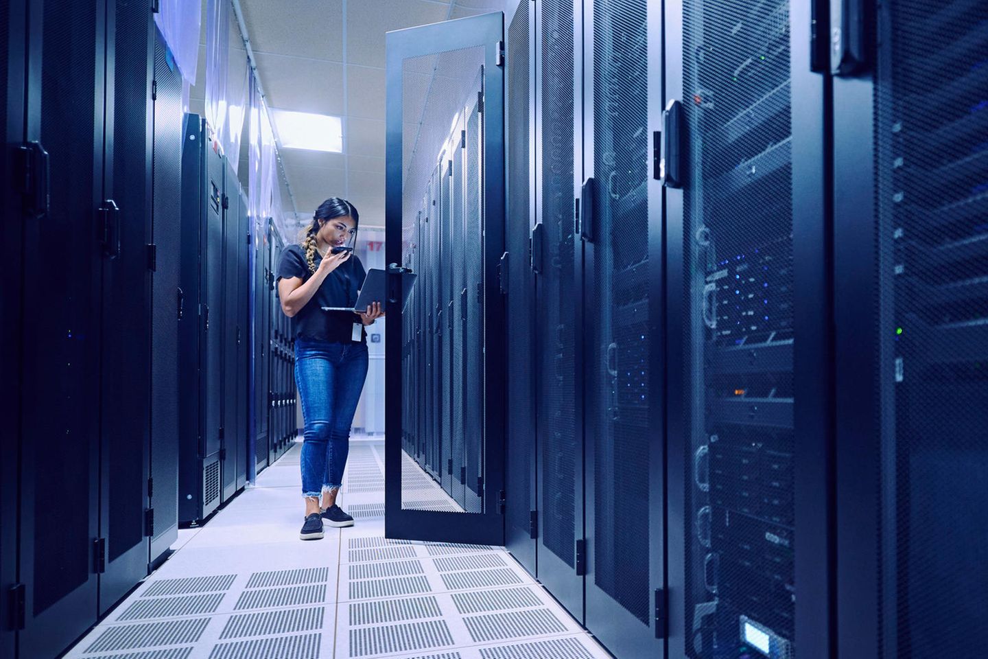 Eine Technikerin arbeitet mit Laptop und Telefon im Serverraum
