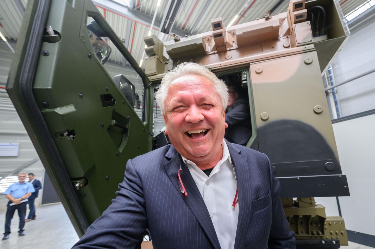 Armin Papperger, Vorstand Rheinmetall, steht lachend vor einer geschützten Fahrerkabine für Logistikfahrzeuge der HX-Serie