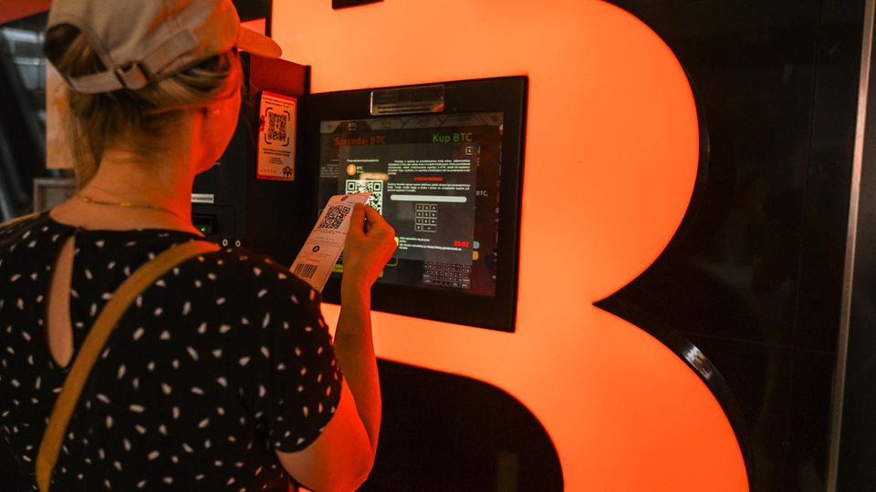 Eine Frau, die vor einem Bitcoin-Automaten die aktuellen Bitcoin-Kurse überprüft Eine Frau, die vor einem Bitcoin-Automaten die aktuellen Bitcoin-Kurse überprüft