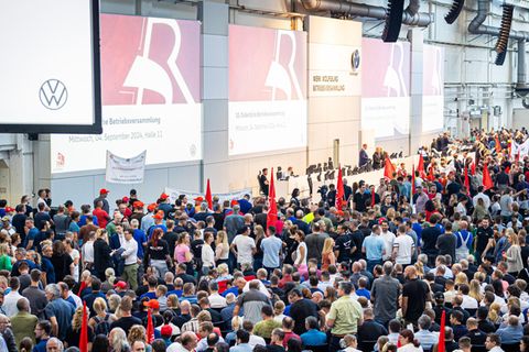 Mitarbeiter warten auf den Beginn einer Betriebsversammlung in einer Halle im VW-Werk