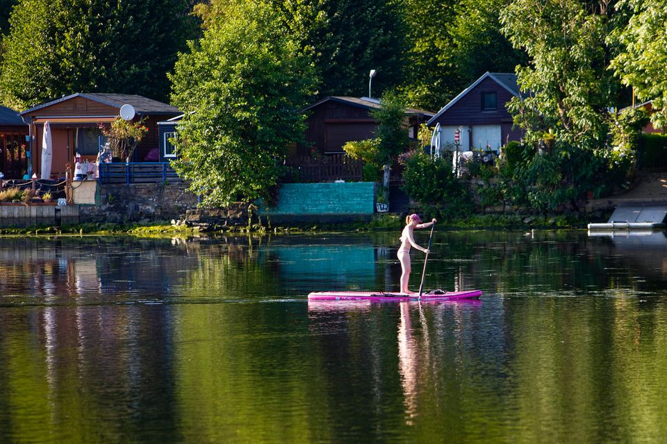 Stand-up-Paddlerin vor Ufer mit Schrebergärten