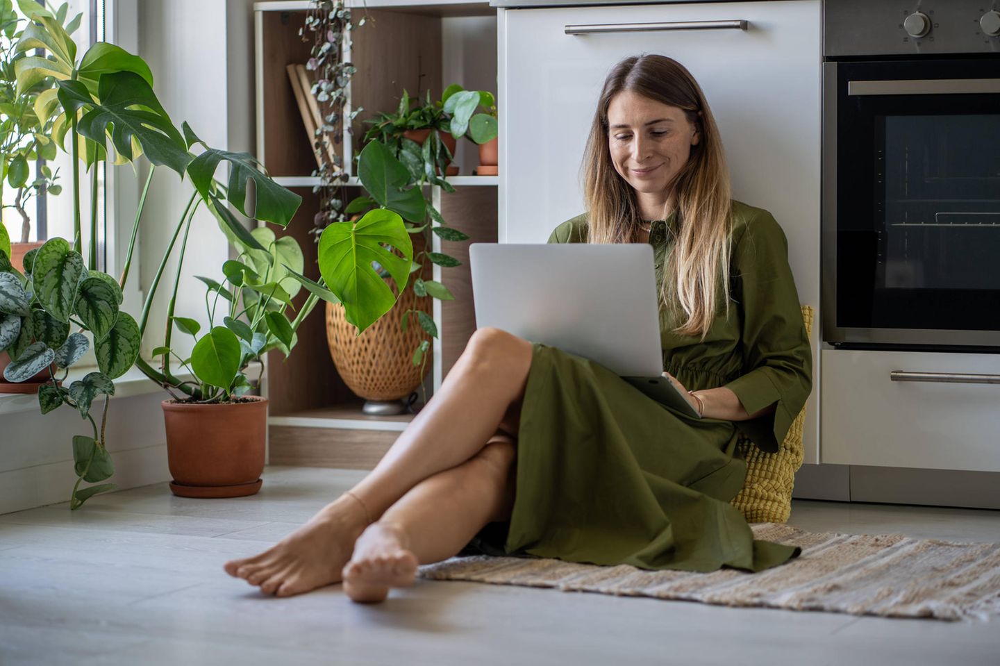 Frau sitzt mit dem Laptop auf dem Küchenboden