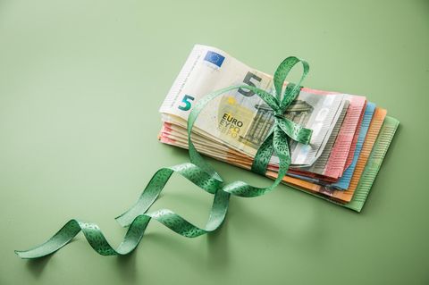 Ein zusammengelegter Geldstapel aus unterschiedlichen Scheinen ist mit einer grünen Schleife zusammengebunden