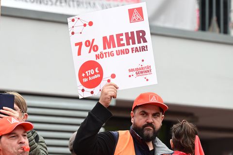 Arbeiter demonstrieren mit Transparenten für eine Forderung von 7 Prozent mehr Lohn