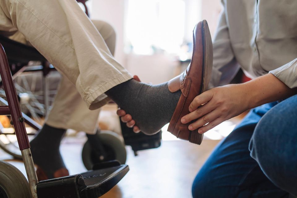 Familienmitglied hilft pflegebedürftigem Angehörigen beim Schuh anziehen