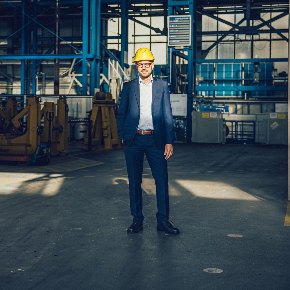 Christian Bruch steht in einer Werkshalle mit einem Helm auf dem Kopf