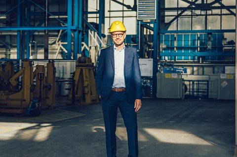 Christian Bruch steht in einer Werkshalle mit einem Helm auf dem Kopf