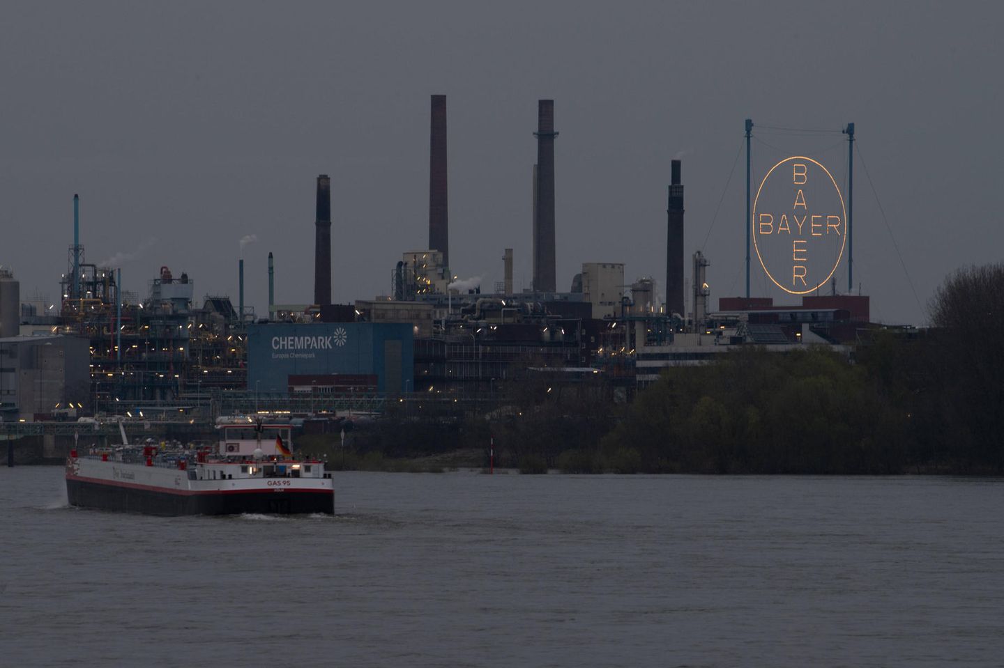 Ein Frachtschiff passiert in der Dämmerung den Chempark in Leverkusen