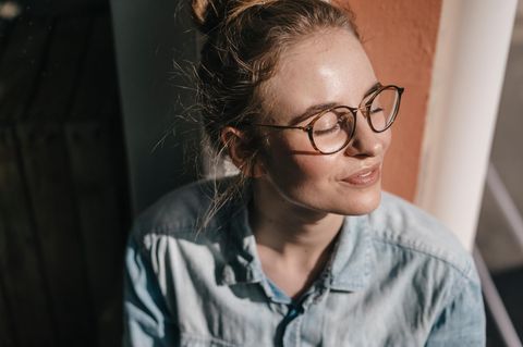 Bebilderung "Selbstkritik" und "innerer Kritiker": Eine junge Frau sitzt mit geschlossenen Augen in der Sonne