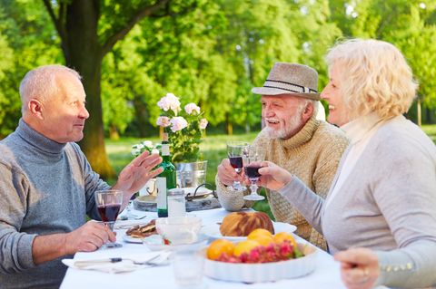Drei ältere Menschen sitzen im Freien bei Wein und Kuchen