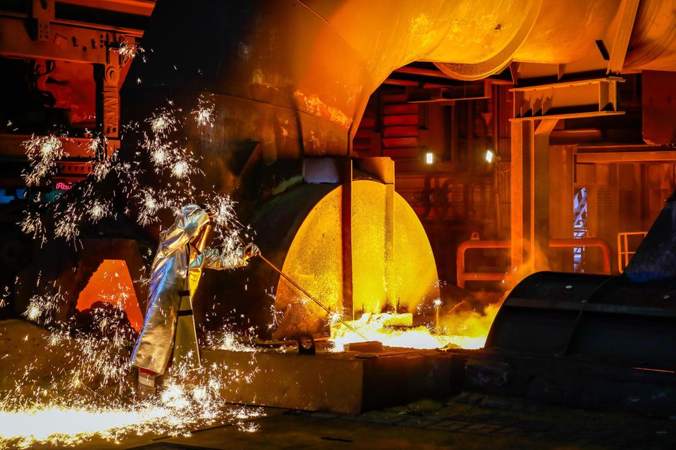 Ein Thyssenkrupp-Stahlarbeiter im Schutzanzug entnimmt eine 1500 Grad heiße Roheisenprobe