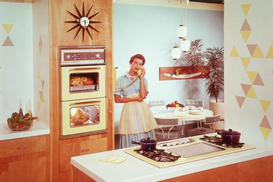 Tradwife: Eine Hausfrau aus den 50ern, steht in ihrer Küche, das Essen im Ofen und telefoniert