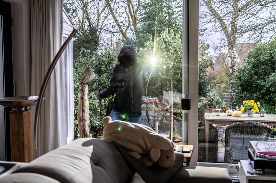 Einbrecher steht auf der Terrasse und schaut ins Haus