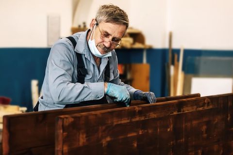 Ein älterer Mann streicht in einer Schreinerei Holzbretter mit dunklem Lack