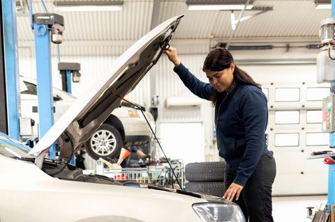 Mechanikerin, die die Motorhaube eines Autos hält