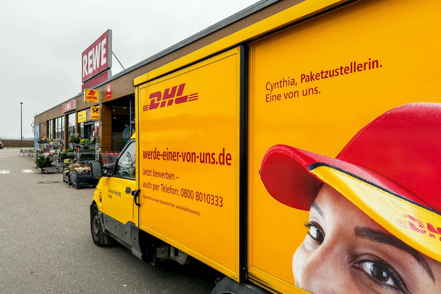 DHL Deutsche Post Zustellfahrzeug mit Mitarbeiter-Werbung vor einem REWE-Markt