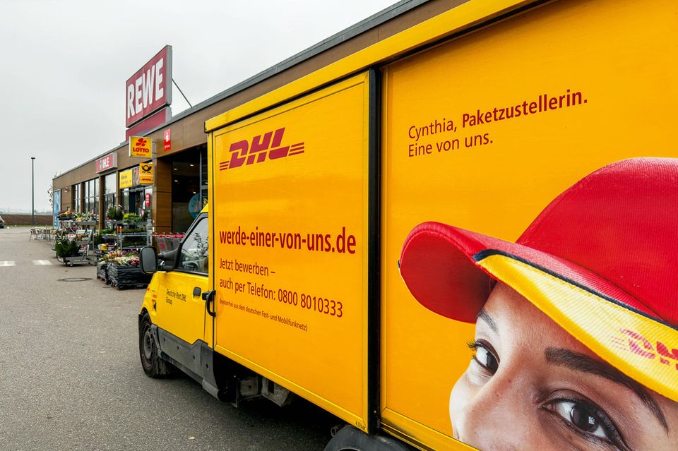 DHL Deutsche Post Zustellfahrzeug mit Mitarbeiter-Werbung vor einem REWE-Markt