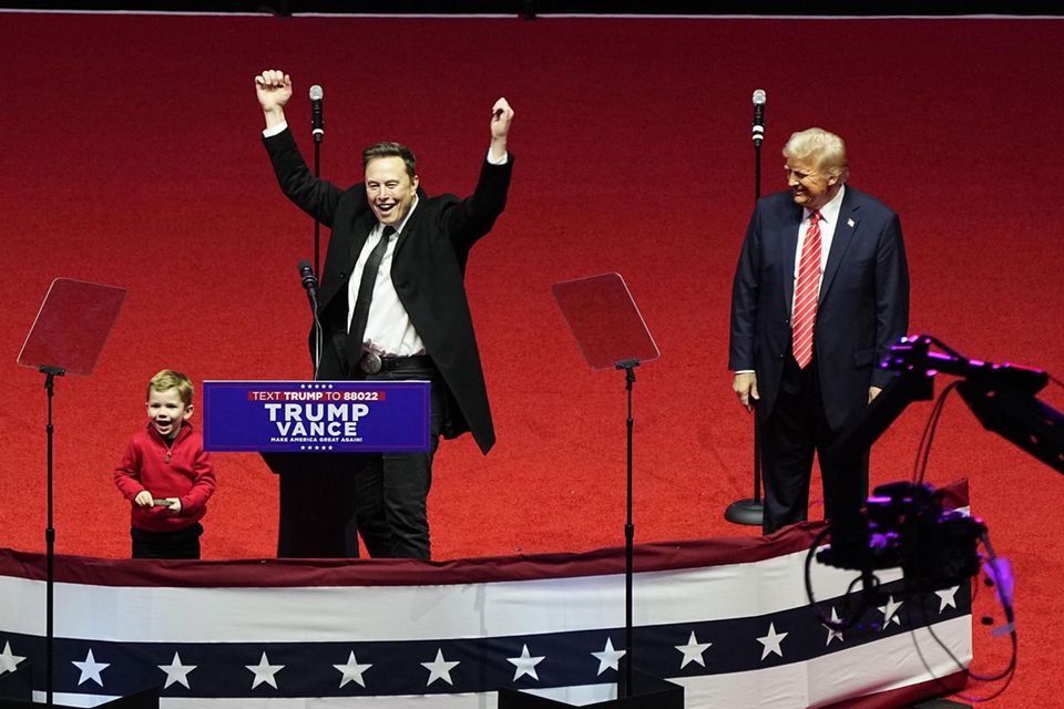 Elon Musk steht vor einem Rednerpult, neben ihm Donald Trump