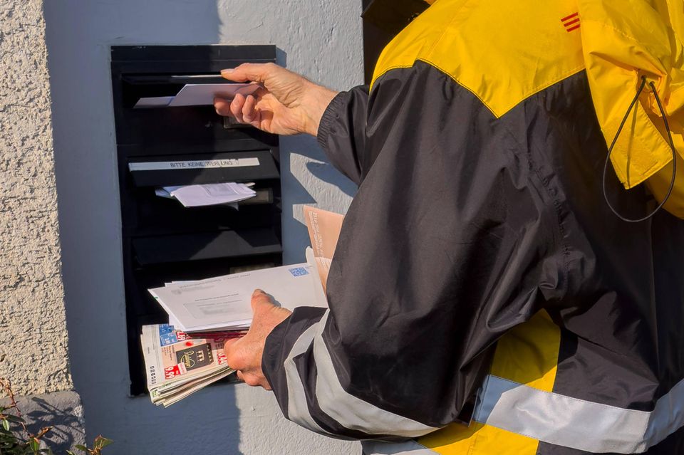 Post vom Finanzamt: Postbote wirft Briefe in den Briefkasten eines Hauses