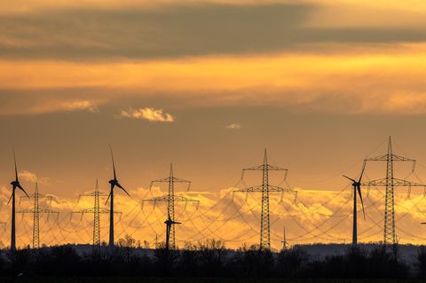Windräder und Stromleitungen stehen im Sonnenuntergang