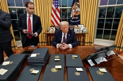 Donald Trump sitzt im Oval Office des Weißen Hauses an seinem Schreibtisch vor vielen Mappen