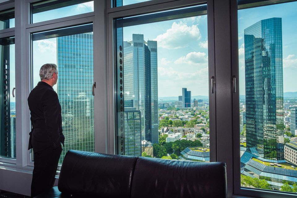 Ein Mann schaut aus dem Fenster auf die Bankentürme von Frankfurt