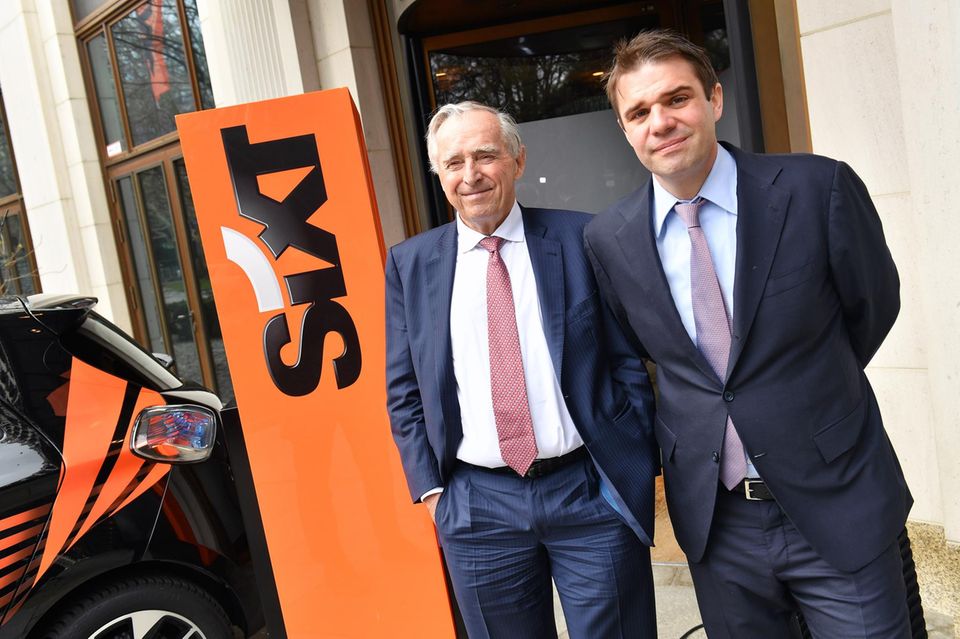 Erich Sixt und Alexander Sixt stehen im Anzug vor einem Firmenschild