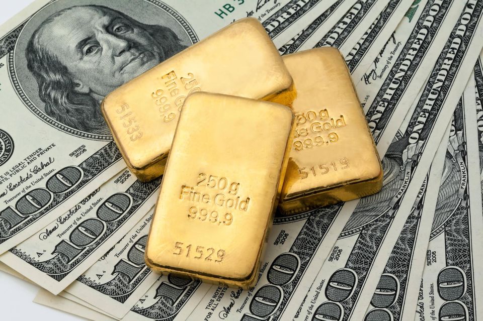 Drei Goldbarren liegen auf aufgefächerten 100-Dollar-Scheinen