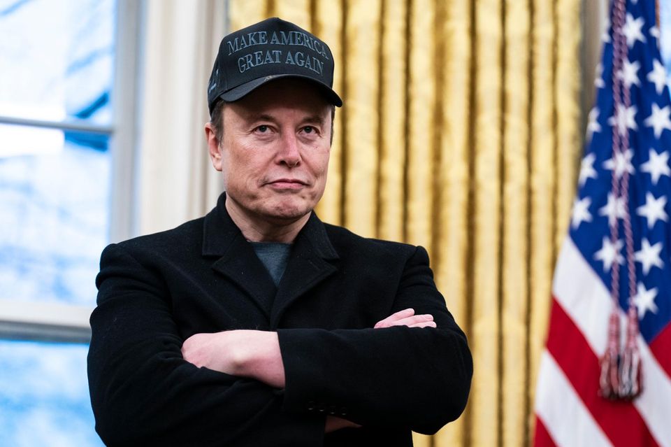 Elon Musk steht mit verschränkten Armen im Oval Officedes Weißen Hauses