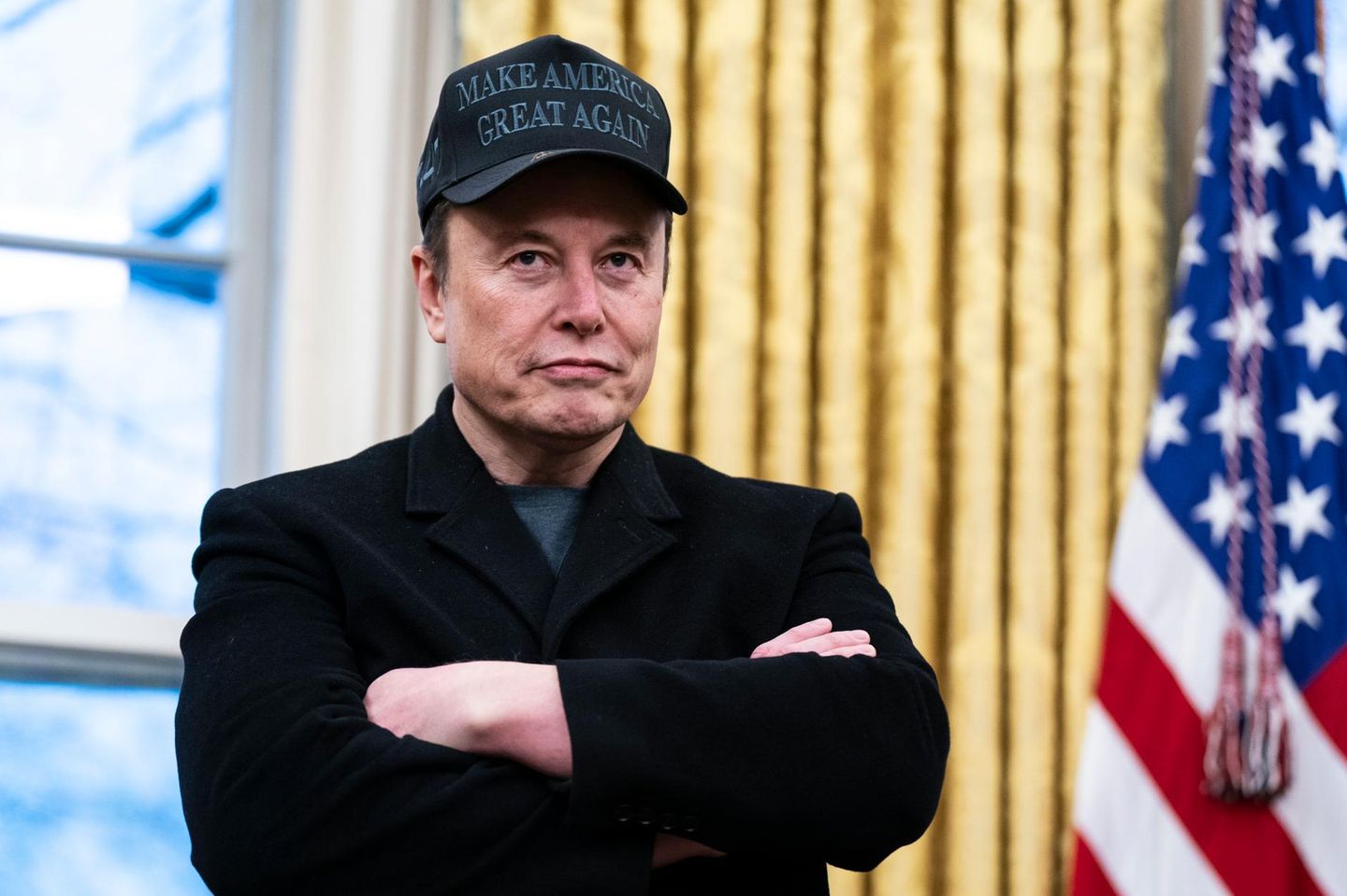 Elon Musk steht mit verschränkten Armen im Oval Officedes Weißen Hauses