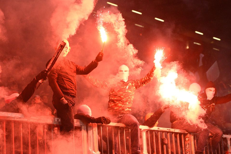 Auf einem Metallzaun im Millerntorstadion sitzen Vermummte und brennen Signalfackeln ab