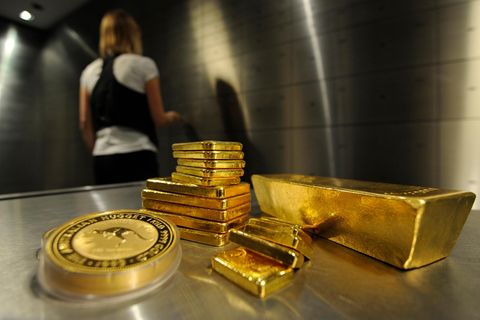 Goldbarren und Münzen liegen in einem Tresorraum, eine Frau schließt sie ein