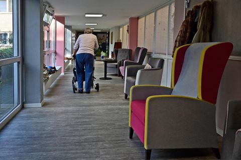 Eine Seniorin geht mit einem Rollator über den Flur eines Pflegeheims
