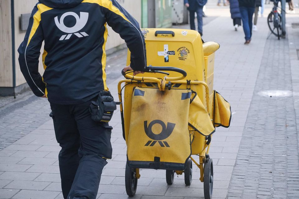 Ein Briefzusteller schiebt seinen Trolley über einen Gehweg
